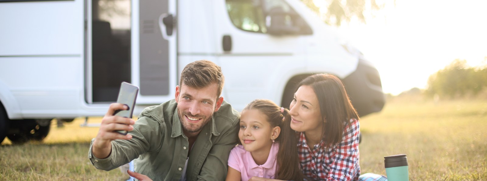 a family of three taking a selfie besides their RV